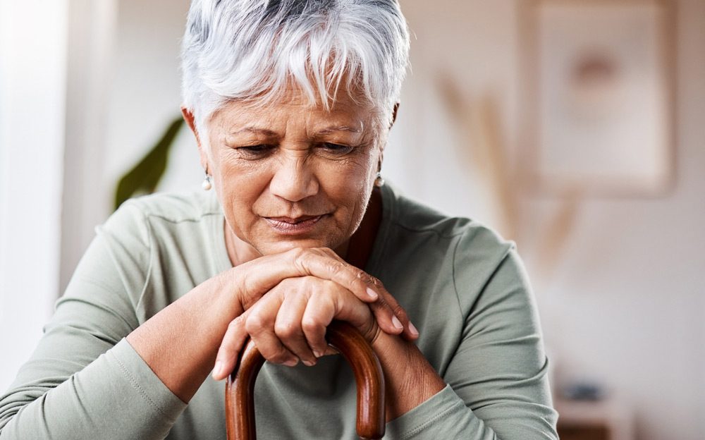 elderly woman leaning on her cane in deep thought.