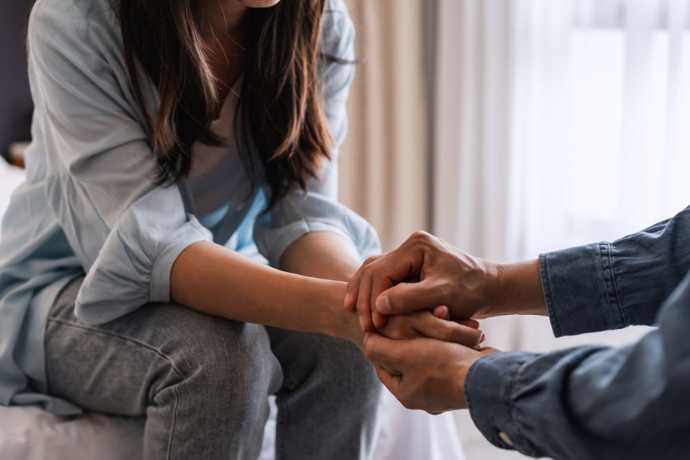 Two people sitting closely, with one person holding the other's hands in a gesture of support and compassion.