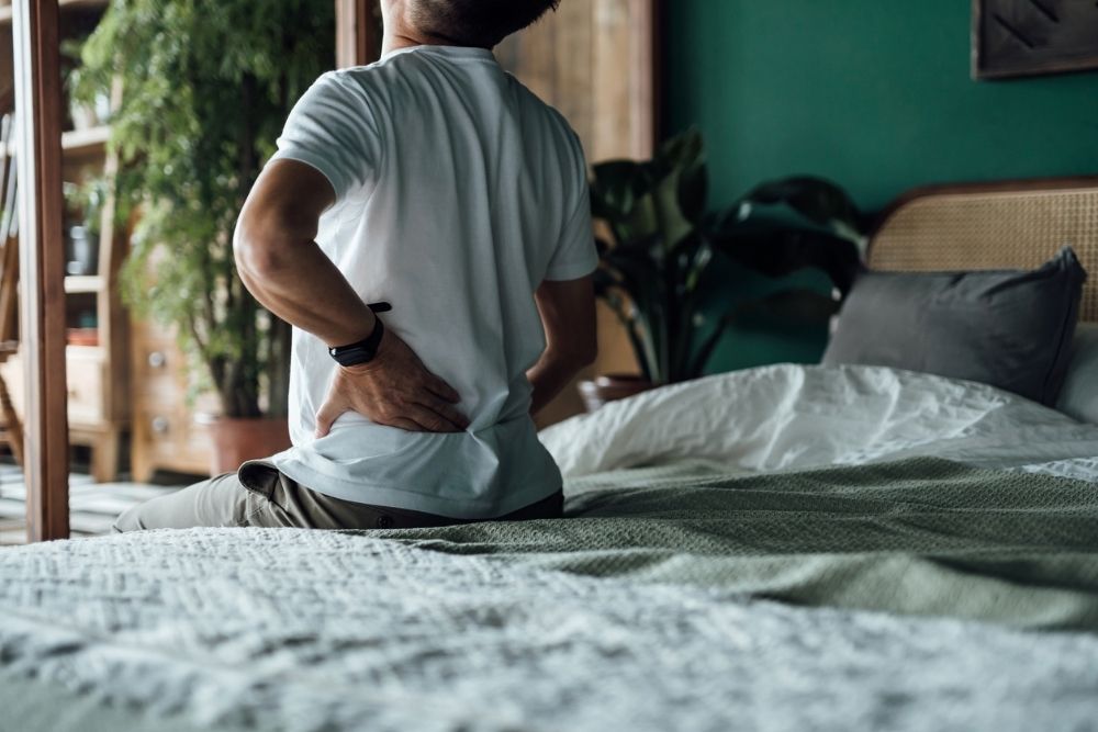 Person sitting on the edge of a bed holding their lower back in pain, illustrating the struggle of chronic pain.
