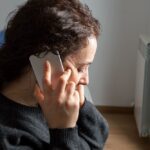 Close-up of Serious woman attending a phone call sitting on a bed in the bedroom