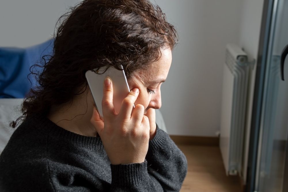 Close-up of Serious woman attending a phone call sitting on a bed in the bedroom