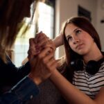 Palms Behavioral Health - How to Create a Support System When You Feel Alone. A young woman holds hands with an older woman while sitting on a coach. The young woman appears appreciative and consoled.